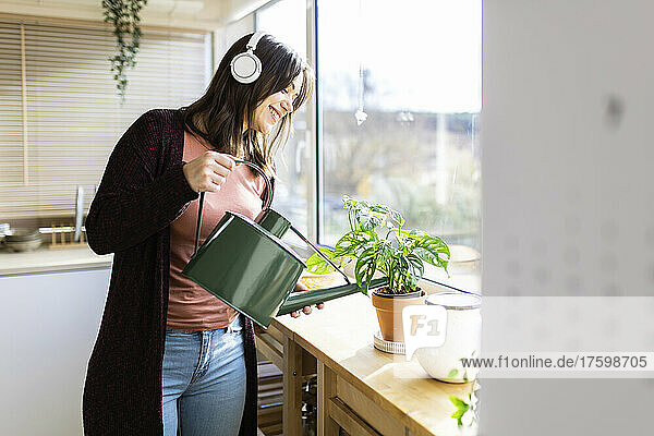 Frau hört Musik und gießt Zimmerpflanze durch Dose zu Hause