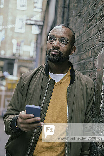 Contemplative man with smart phone leaning on wall
