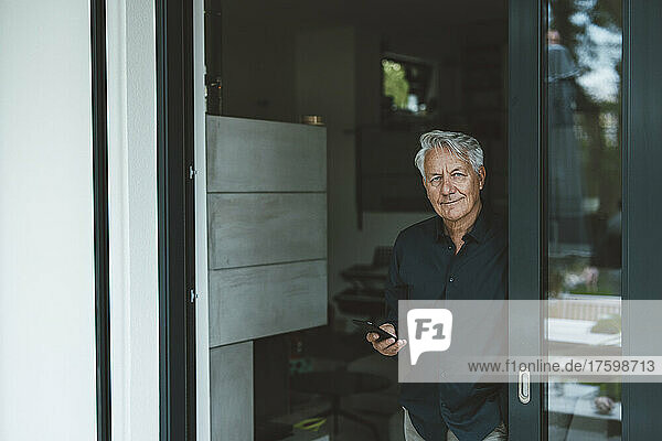 Senior man with smart phone standing at doorway