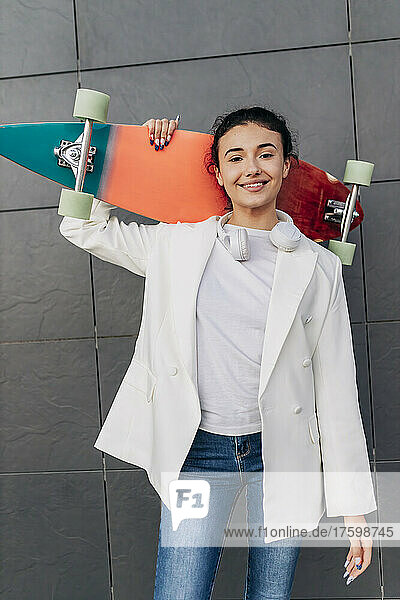 Young woman holding skateboard in front of wall