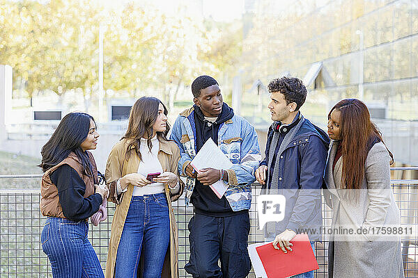 Multiracial students talking by railing at university campus