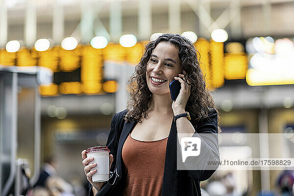 Lächelnde Frau mit Einwegkaffeetasse  die auf dem Smartphone spricht