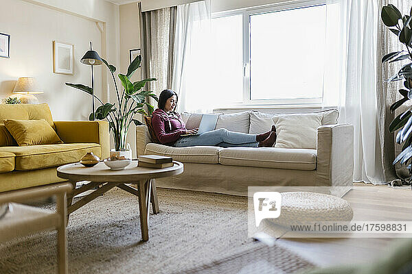 Young woman using laptop sitting on sofa in living room