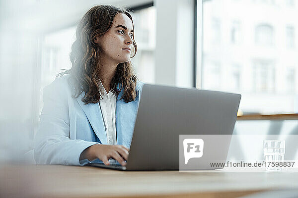 Thoughtful businesswoman with laptop sitting at desk in office