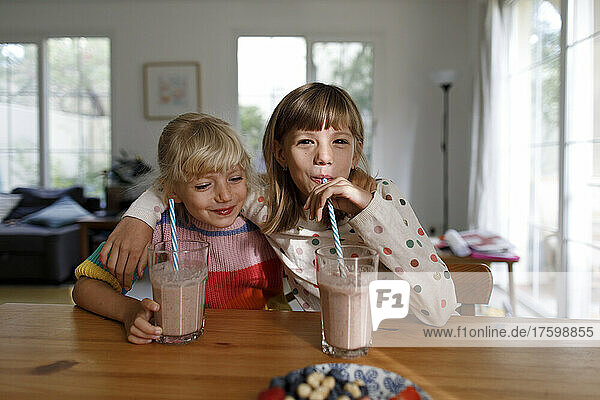 Happy sisters drinking smoothie at home