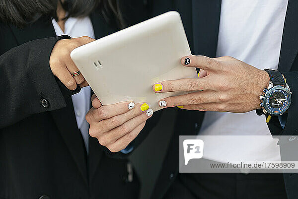 Businessman with painted nail using tablet PC with colleague