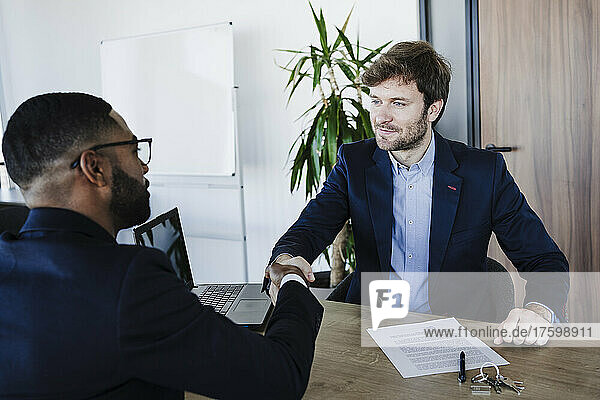 Geschäftsmann schüttelt dem Kunden die Hand  nachdem er im Büro den Vertrag unterzeichnet hat