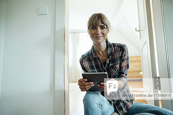 Smiling woman with bangs holding digital tablet at home