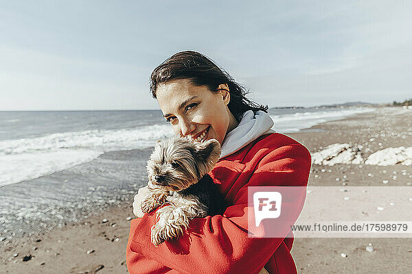Smiling woman carrying Yorkshire terrier at beach