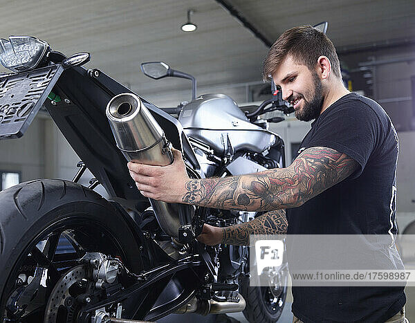 Tattooed mechanic examining exhaust pipe of motorcycle in workshop