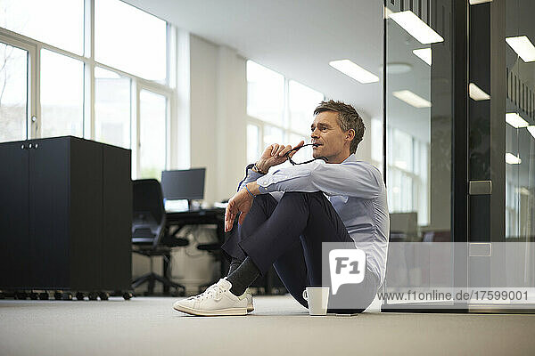 Nachdenklicher Geschäftsmann mit Kaffeetasse sitzt auf dem Boden im Büro