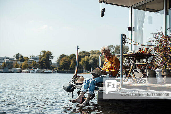 Senior man reading newspaper sitting at houseboat on sunny day
