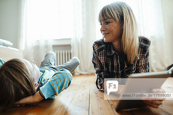 Mother with tablet PC looking at son lying on floor at home