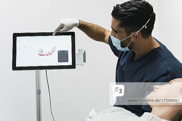 Dentist showing teeth X-ray to patient over intraoral scanner screen in clinic