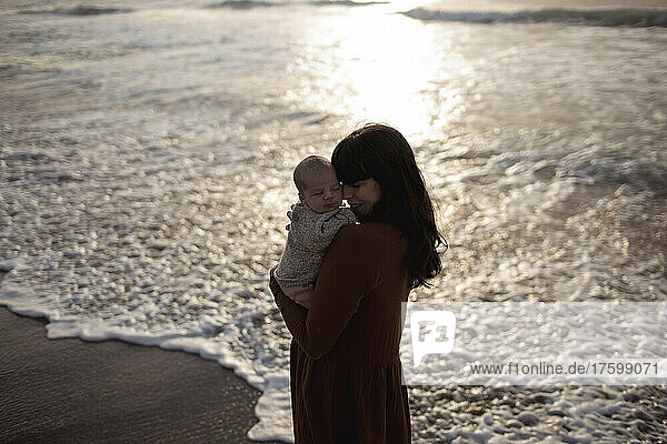 Loving mother embracing innocent baby boy at sunrise