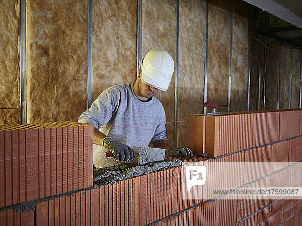 Bricklayer applying cement on bricks with hand tool at construction site