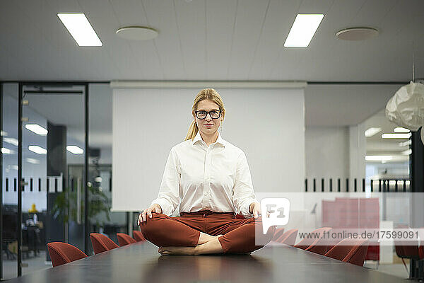 Confident businesswoman sitting on conference table in meeting room at modern office