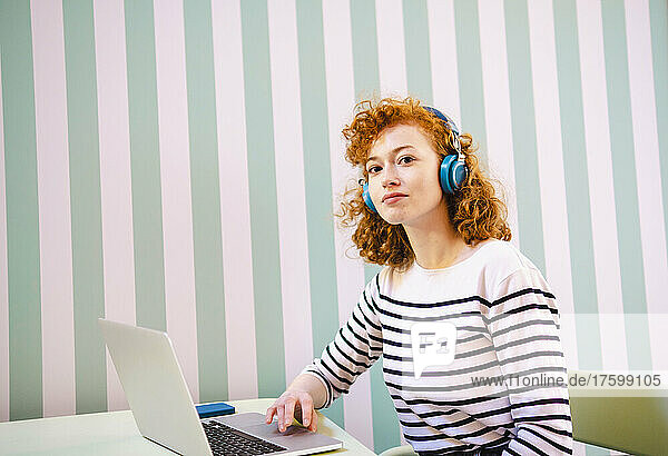 Young woman with laptop listening music through headphones in cafe
