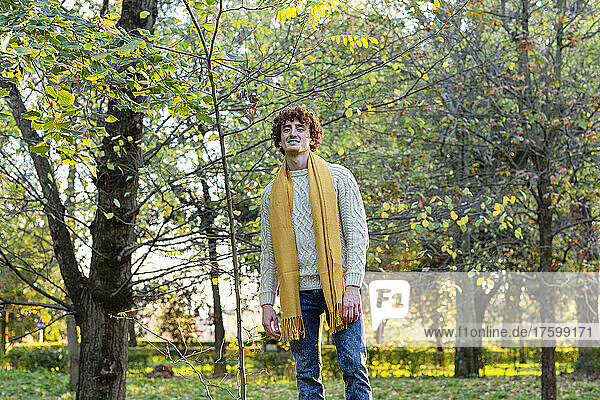 Young man with yellow scarf standing at autumn park