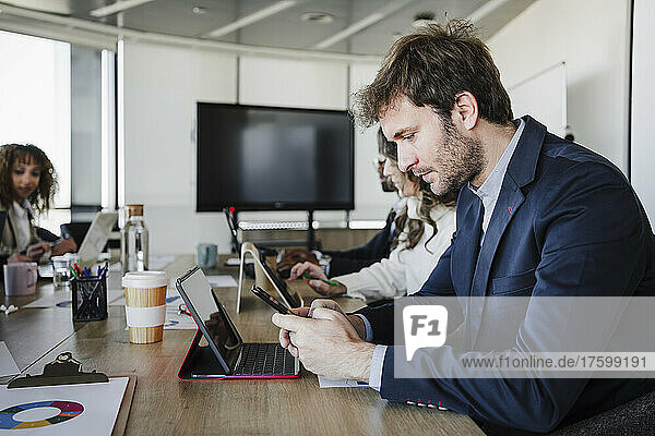 Businessman using smart phone sitting by colleagues at desk in office