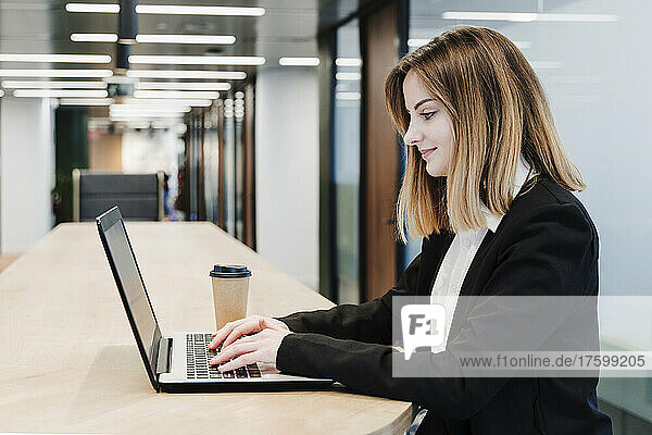 Smiling businesswoman using laptop on table in office