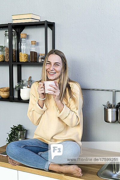 Smiling woman with coffee cup sitting in kitchen at home