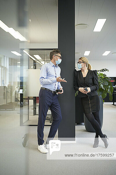 Businessman and businesswoman wearing protective face masks and talking in office