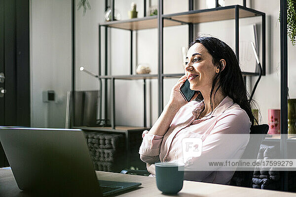 Smiling businesswoman talking on mobile phone in coworking office