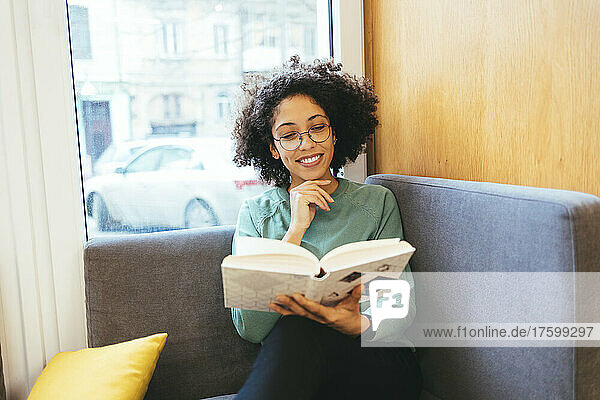 Smiling woman reading book sitting on sofa