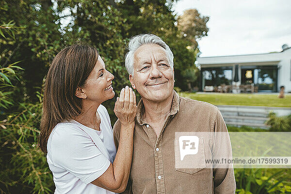 Smiling woman whispering in senior man's ear at backyard