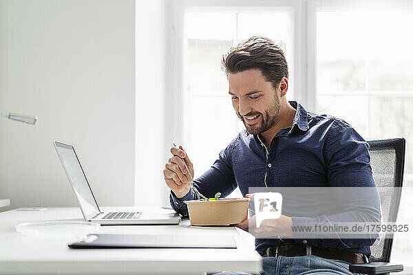 Smiling businessman having salad at desk in office