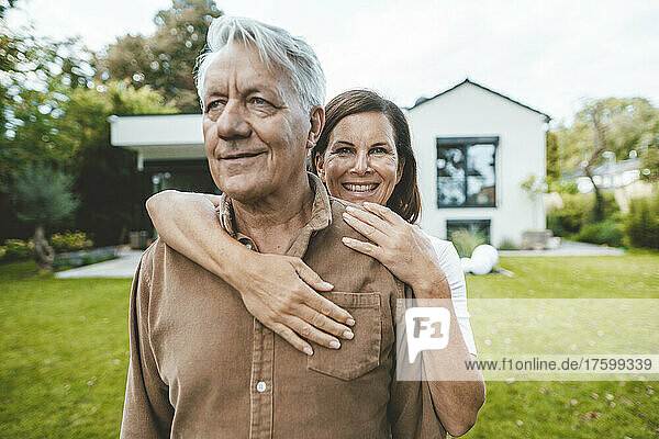 Glückliche Frau umarmt älteren Mann von hinten im Hinterhof