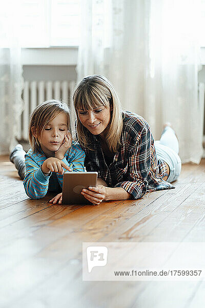 Son pointing at digital tablet with mother lying on floor at home