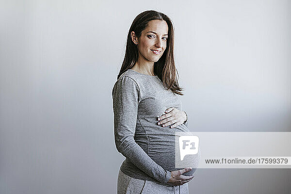 Pregnant woman holding belly standing in front of wall