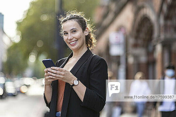 Happy businesswoman with smart phone on city street