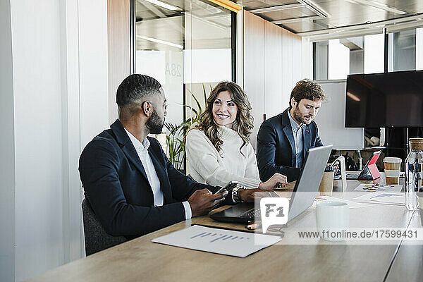 Smiling young businesswoman discussing with colleague sitting at desk in office