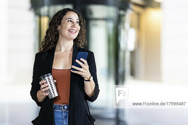 Smiling businesswoman with reusable cup and smart phone