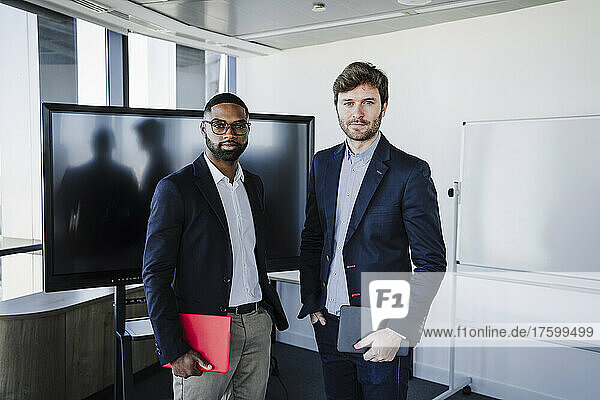 Businessmen holding tablet PC standing with hands in pockets at coworking office