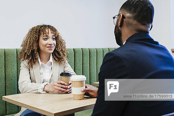 Lächelnde Geschäftsfrau schaut Kollegen bei der Kaffeepause im Coworking-Büro an