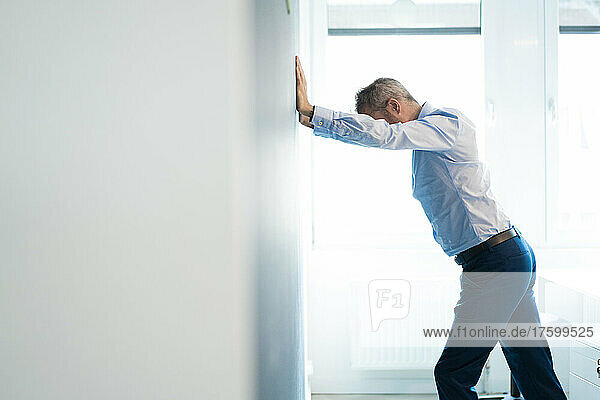 Tired businessman leaning on wall stretching at workplace