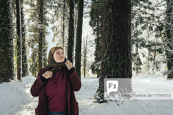 Contemplative woman wearing scarf standing in winter forest