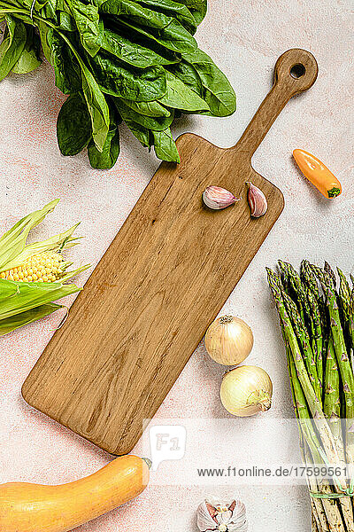 Studio shot of assorted vegetables surrounding cutting board