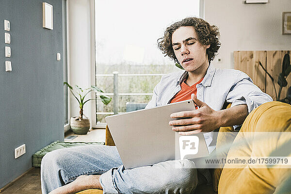 Young man with brown hair using laptop sitting on sofa at home