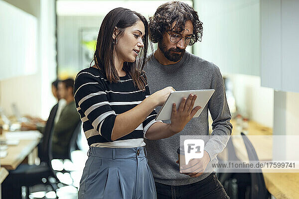 Creative businesswoman explaining businessman on tablet PC in coworking office