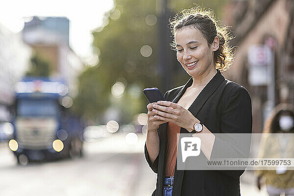 Smiling businesswoman using mobile phone in city