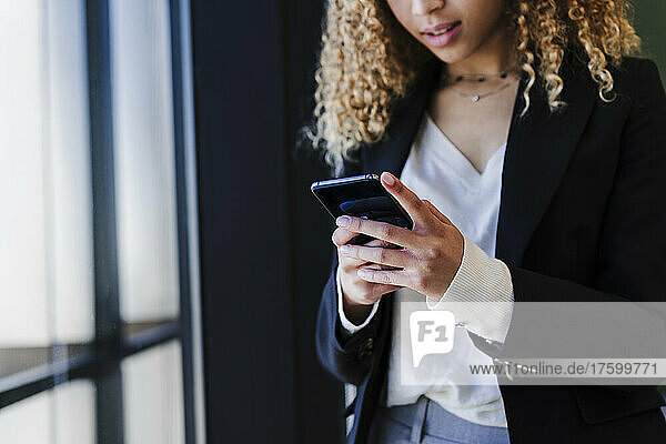 Junge Geschäftsfrau benutzt Mobiltelefon im Büro