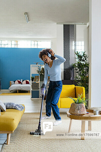 Cheerful young woman enjoying music and cleaning carpet in living room