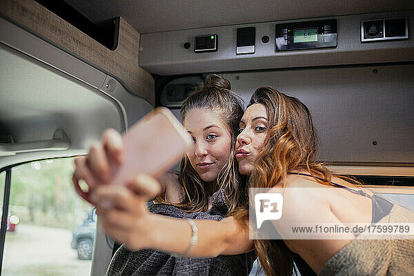 Friends taking selfie on smart phone in motor home on weekend