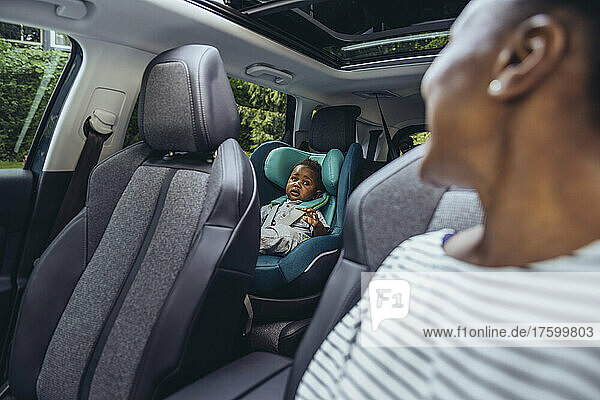 Mother looking at baby boy sitting in car