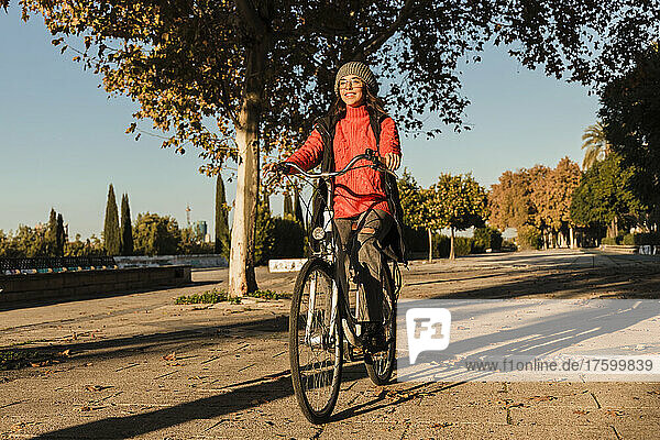 Cheerful young woman cycling on footpath
